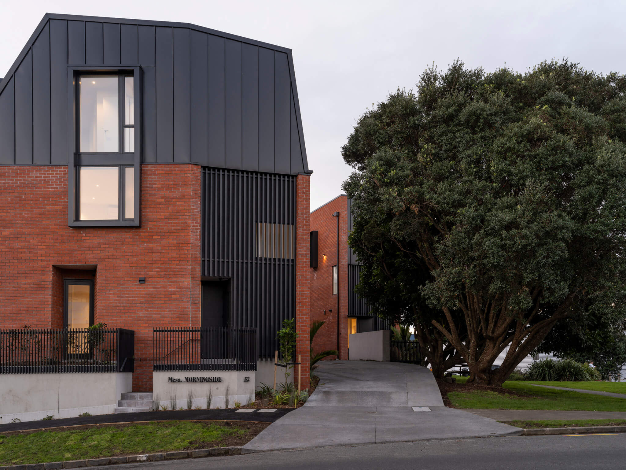 Front elevation of Mesa Morningside Auckland townhouses garage and entrance crafted in industrial looking clay brick and black metal