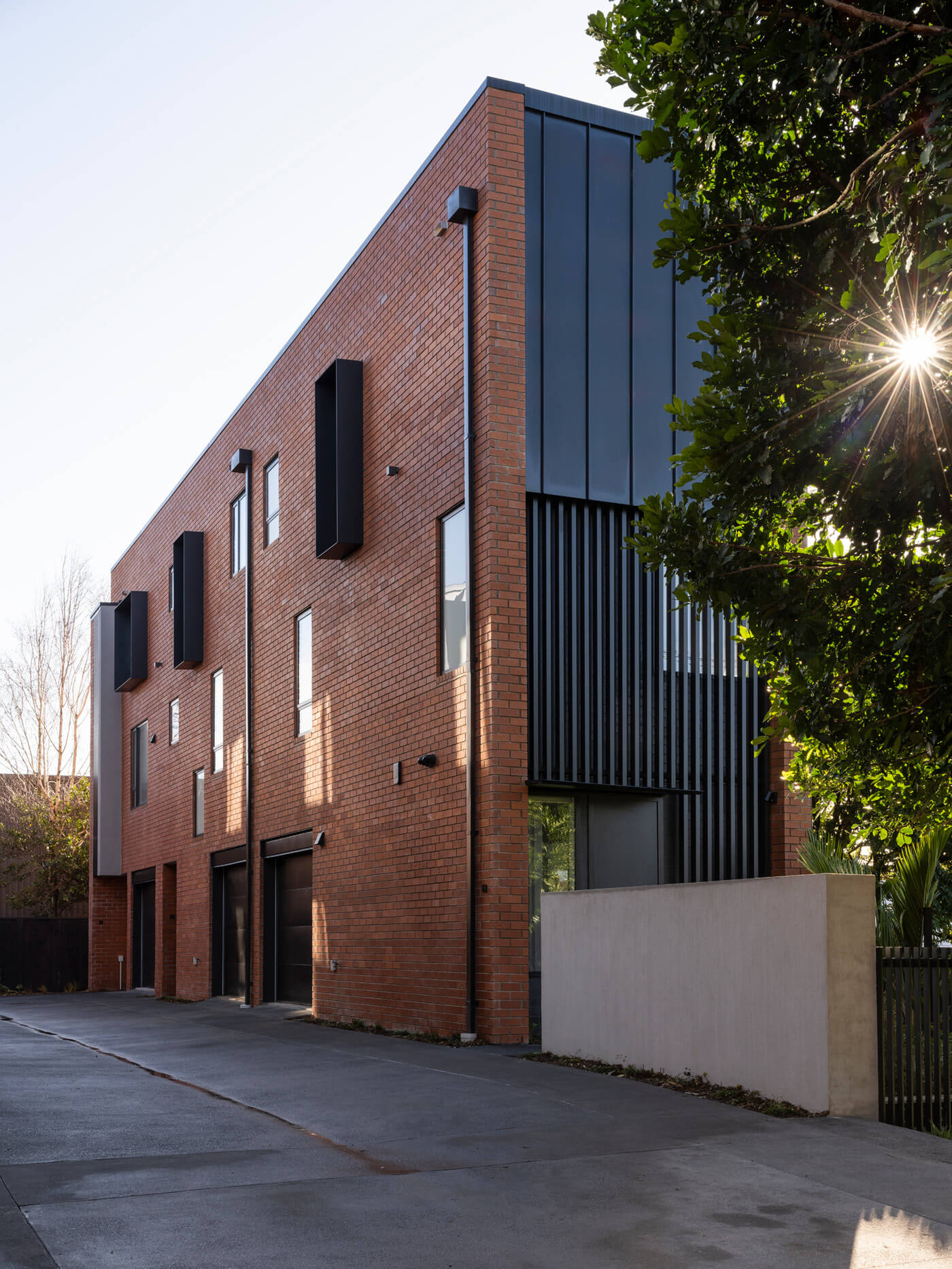 East side facade of Mesa Morningside Auckland townhouses garage and entrance crafted in industrial looking clay brick and black metal